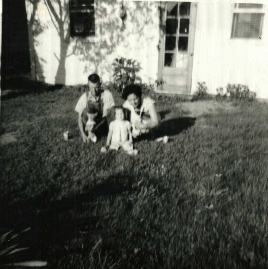 Elmer and Mary Doan kneeling in the grass behind Phyllis Louise and a small dog, July 1960